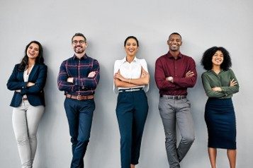 Diverse group of five professionals standing confidently against a grey background.