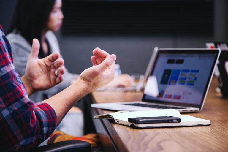 Hands gesturing during a discussion at a meeting table with a laptop and notebook.