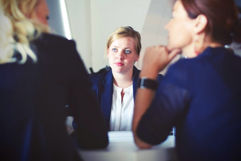 A woman in a blazer attentively listens during a discussion with others.