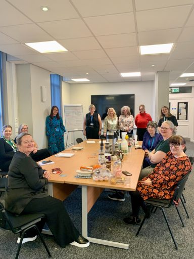 Group of people gathered around a table in an office setting, smiling and engaged.